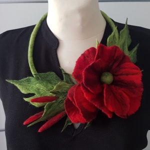 Puede incluir: Una flor roja de fieltro con hojas verdes de fieltro, unida a un collar de fieltro marrón. La flor es una amapola con un centro rojo oscuro.