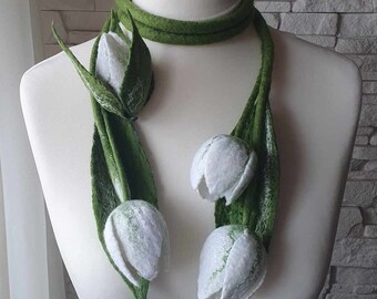 Può includere: Una sciarpa di feltro verde con fiori di feltro bianco che ricordano i tulipani. La sciarpa è drappeggiata su un manichino bianco.