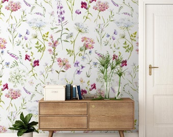 May include: A wooden dresser with three drawers, featuring a floral wallpaper with pink, purple, and green flowers. The dresser is in a room with a white door and a potted plant.
