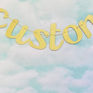May include: Gold glitter custom banner with the word "custom" spelled out. The banner is hanging against a light blue and white background.