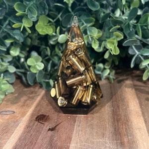May include: A pyramid-shaped resin sculpture filled with gold-colored bullet casings. The sculpture is on a wooden surface.