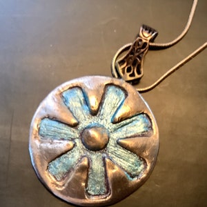 Peut inclure: Un collier avec un pendentif en argent rond, orn&eacute; d'une fleur bleue et argent&eacute;e. Le pendentif a un centre sur&eacute;lev&eacute; et six p&eacute;tales.