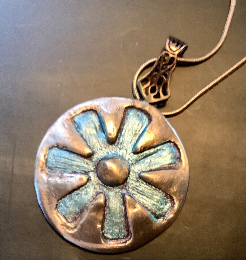 Peut inclure: Un collier avec un pendentif en argent rond, orn&eacute; d'une fleur bleue et argent&eacute;e. Le pendentif a un centre sur&eacute;lev&eacute; et six p&eacute;tales.