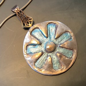 Peut inclure: Un collier avec un pendentif rond en argent, de forme florale, bleu et or. Le pendentif a un centre sur&eacute;lev&eacute; et huit pointes.
