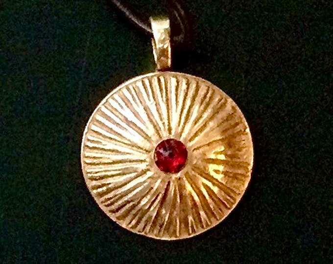 AI 9. Handmade bronze pendant in the shape seen on African shields, hung from 18” brown leather cord, manmade garnet gem in the center