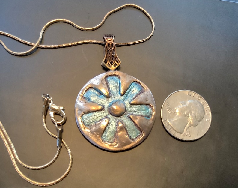 Peut inclure: Un collier avec un pendentif rond en argent, orn&eacute; d'une fleur bleue et argent&eacute;e. Le pendentif est &agrave; peu pr&egrave;s de la taille d'une pi&egrave;ce de 25 centimes d'euro.