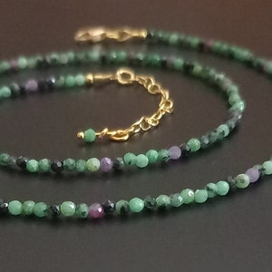 Könnte beinhalten: Ein grünes und schwarzes Edelstein-Halsketten- und Armband-Set mit goldenen Akzenten. Die Halskette und das Armband bestehen aus kleinen, runden Perlen.