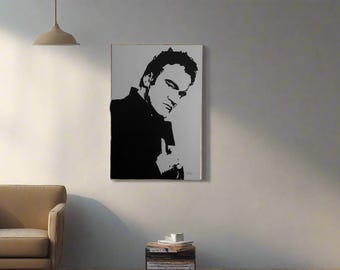 May include: Black and white portrait of a man on a white background. The artwork is framed and hangs on a light-colored wall. The man is wearing a dark jacket and is looking towards the viewer. A sofa and side table are in the foreground.