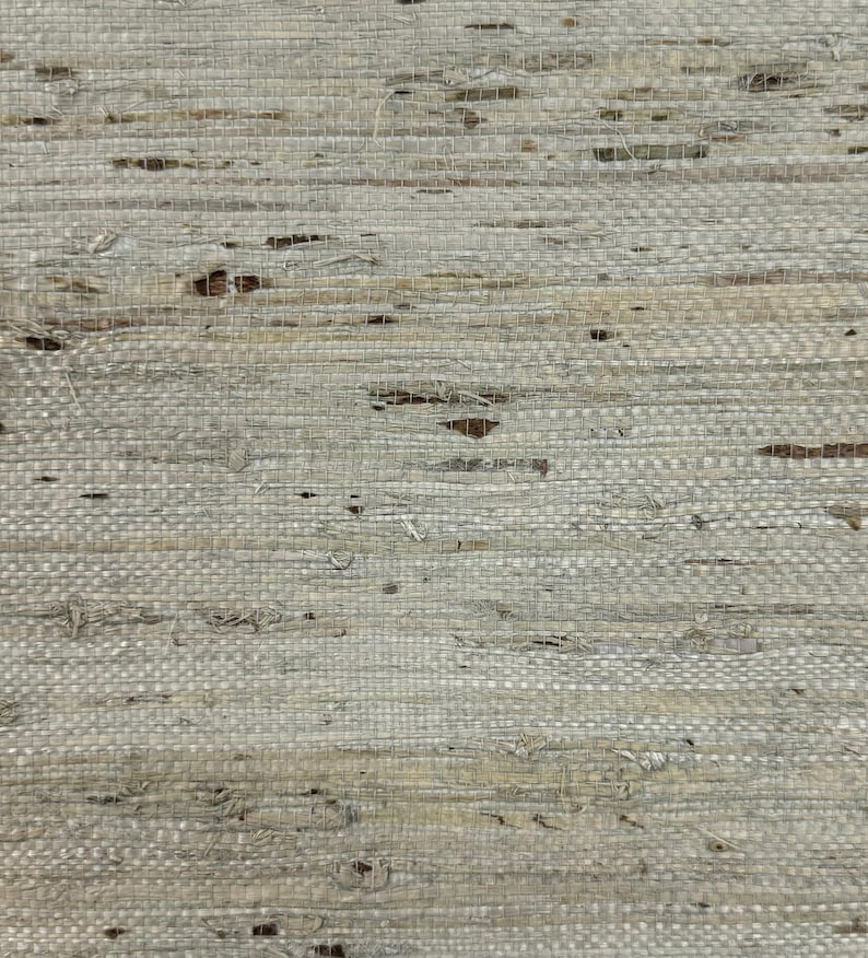 Puede incluir: Primer plano de un textil tejido con un aspecto natural y texturizado. El material es principalmente gris claro con sutiles variaciones de tono y peque&ntilde;as manchas marrones oscuras. El tejido es visible, creando un patr&oacute;n similar a una cuadr&iacute;cula.
