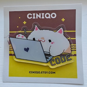 May include: A clear acrylic pin featuring a pixel art white cat typing on a gray laptop with a black heart icon. The pin displays the text CODE and is mounted on a square backing card with the text CINIQO and CINIQO.ETSY.COM printed on it.