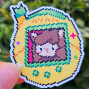 May include: A pixelated sticker of a brown alpaca wearing a yellow, green, and red digital pet device.