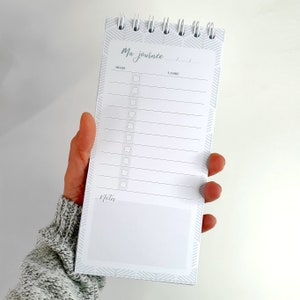 Peut inclure: Un carnet à spirales blanc avec un motif chevron gris sur la couverture. Le carnet porte l'inscription "Ma journee" sur la première page. Le carnet comporte une liste de choses à faire et une section pour les notes.