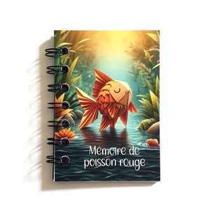 Pode incluir: Um caderno de espiral com uma ilustração colorida de um peixe dourado em um lago. A capa apresenta o texto "Mémoire de poisson rouge".