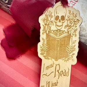 May include: Wooden bookmark featuring a skeleton holding a book with roses and the text "I must Read or I'll just Die."