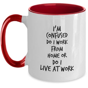 May include: White coffee mug with a red rim and handle. The mug has black text that reads "I'm confused do I work from home or do I live at work."