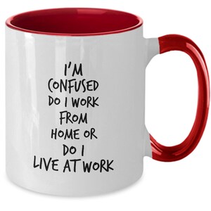 May include: White coffee mug with a red rim and handle. The mug has black text that reads "I'm confused do I work from home or do I live at work."