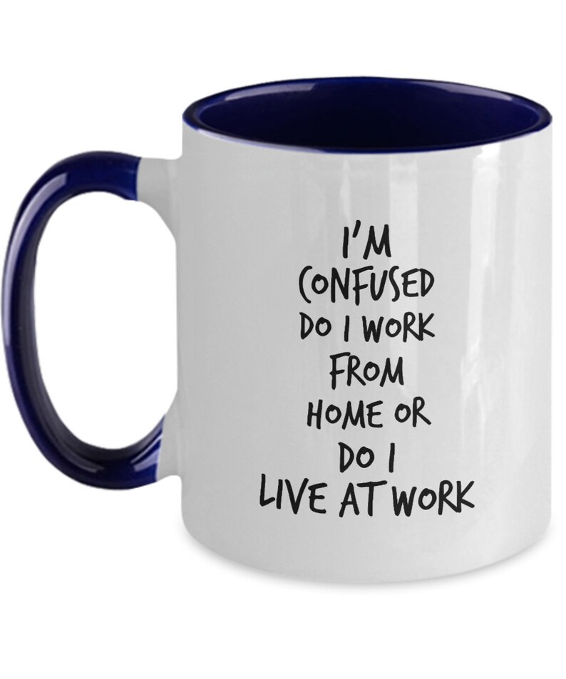 May include: White ceramic coffee mug with a blue rim and handle. The mug has black text that reads "I'm confused do I work from home or do I live at work."
