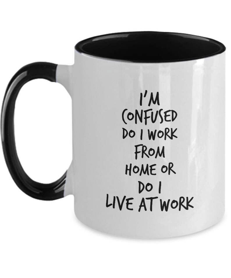 May include: White coffee mug with a black rim and handle. The mug has black text that reads "I'm confused do I work from home or do I live at work."