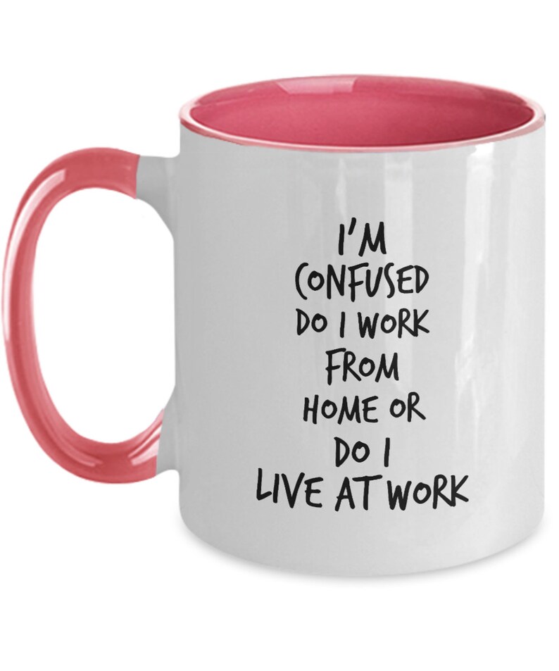 May include: White coffee mug with a pink rim and handle. The mug has black text that reads "I'm confused do I work from home or do I live at work."