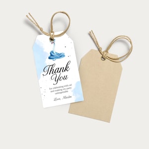K&ouml;nnte beinhalten: Zwei Geschenkanh&auml;nger mit Bindfaden. Einer ist wei&szlig; mit einem blauen Aquarelldesign und dem Schriftzug "Thank You" in eleganter Schrift. Der Anh&auml;nger enth&auml;lt auch den Text "for celebrating with us! and making my party unforgettable Love, Marten". Der zweite ist braun.