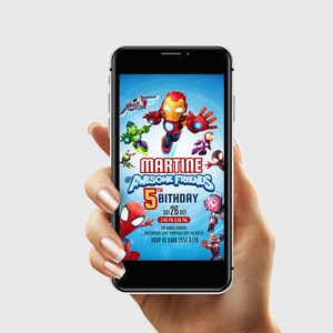 Puede incluir: Un smartphone muestra una invitaci&oacute;n de cumplea&ntilde;os con superh&eacute;roes de dibujos animados. La invitaci&oacute;n dice "Martine & Awesome Friends 5th Birthday" con la fecha, hora y lugar. El tel&eacute;fono se sostiene en una mano.