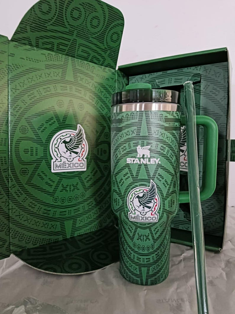 Puede incluir: Una taza de cer&aacute;mica blanca con asa negra y el texto "But First, Coffee" en negrita negra. La taza se encuentra sobre un fondo borroso, sugiriendo un ambiente acogedor.