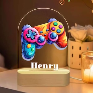 Könnte beinhalten: Ein buntes, regenbogenfarbenes Videospiel-Controller-Nachtlicht mit dem Namen "Henry" darunter. Das Licht befindet sich auf einem weißen Sockel.