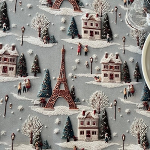 May include: A light blue fabric featuring an embroidered winter scene with white houses, snow-covered ground, evergreen trees, street lamps, and a central copper-colored Eiffel Tower. A stack of white ceramic plates sits on the right side.