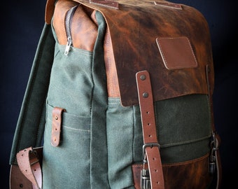 Könnte beinhalten: Ein grüner Canvas-Rucksack mit braunen Lederelementen und Schnallen. Der Rucksack hat ein großes Hauptfach und eine kleinere Fronttasche. Das Leder ist abgenutzt und hat einen Vintage-Look.