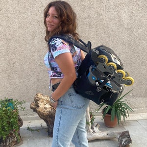 May include: A woman wearing a blue and white patterned shirt and light blue jeans is carrying a black backpack with inline skates attached to it.