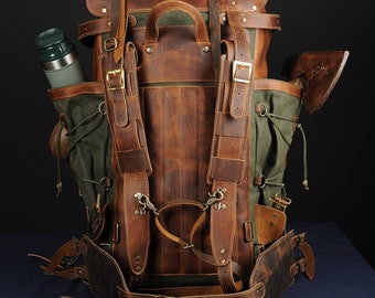 May include: A brown leather and green canvas backpack with adjustable straps and buckles. The backpack has a large main compartment and several smaller pockets. It also has a leather strap with a buckle that can be used to attach an axe or other tools.