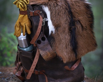 May include: A brown leather backpack with a fur flap, brown leather straps, and a metal buckle. A pair of yellow leather gloves are attached to the side of the backpack.