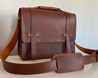 May include: A brown leather messenger bag with a long adjustable strap. The bag has a flap closure with two buckles and a top handle.