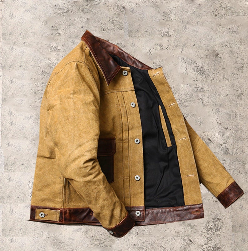 May include: A tan canvas jacket with brown leather trim on the collar, cuffs, and bottom hem. The jacket has a button-up front and multiple pockets.