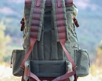 May include: A large green canvas backpack with brown leather straps and buckles. The backpack has a large main compartment and two smaller side pockets.