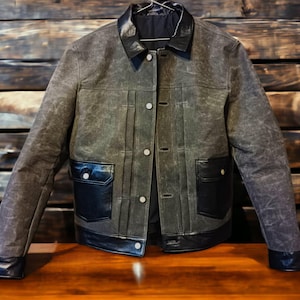 May include: A dark gray denim jacket with black leather trim and pockets. The jacket has a button closure and a collar.