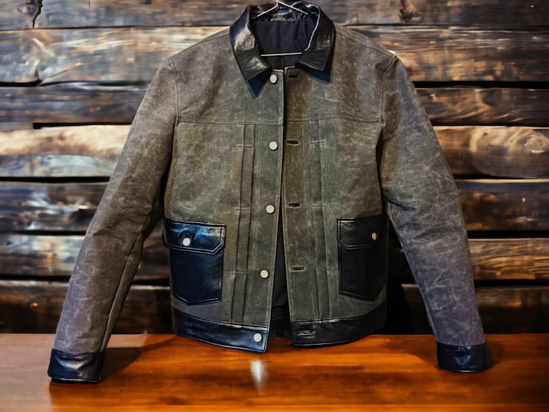 May include: A dark gray denim jacket with black leather trim and pockets. The jacket has a button closure and a collar.