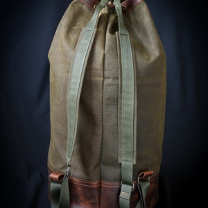 May include: A green canvas duffel bag with brown leather trim and adjustable straps. The bag has a drawstring closure and a large capacity.