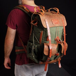 May include: A green canvas and brown leather backpack with multiple pockets and straps.