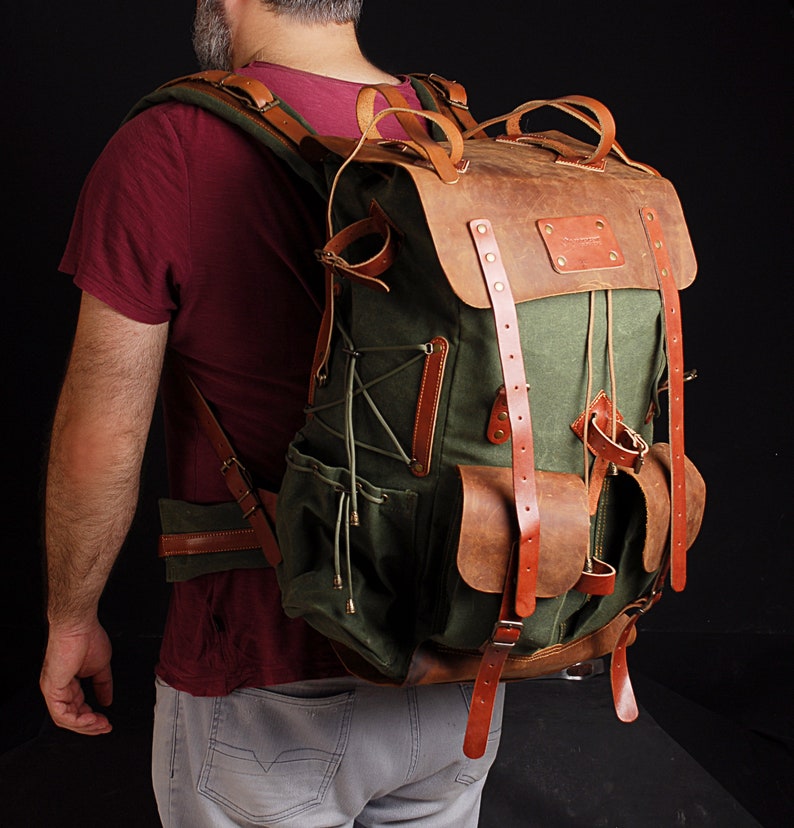 May include: A green canvas and brown leather backpack with multiple pockets and straps.