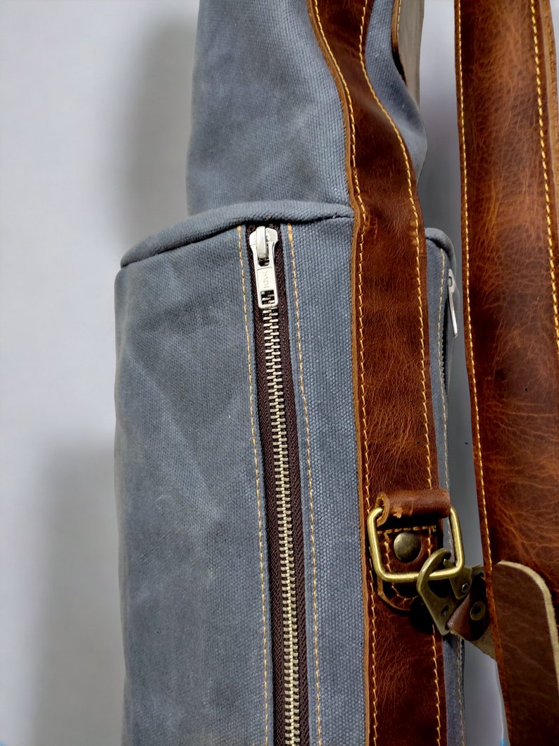 May include: A gray canvas bag with a brown leather strap and a zipper closure. The bag has a brown leather trim and a brass buckle.