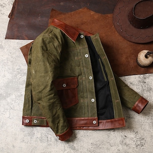 May include: A green denim jacket with brown leather trim. The jacket has a button closure, two pockets, and a brown leather collar.