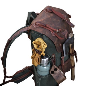 May include: A green canvas and brown leather backpack with a water bottle, gloves, and an axe attached to the outside.