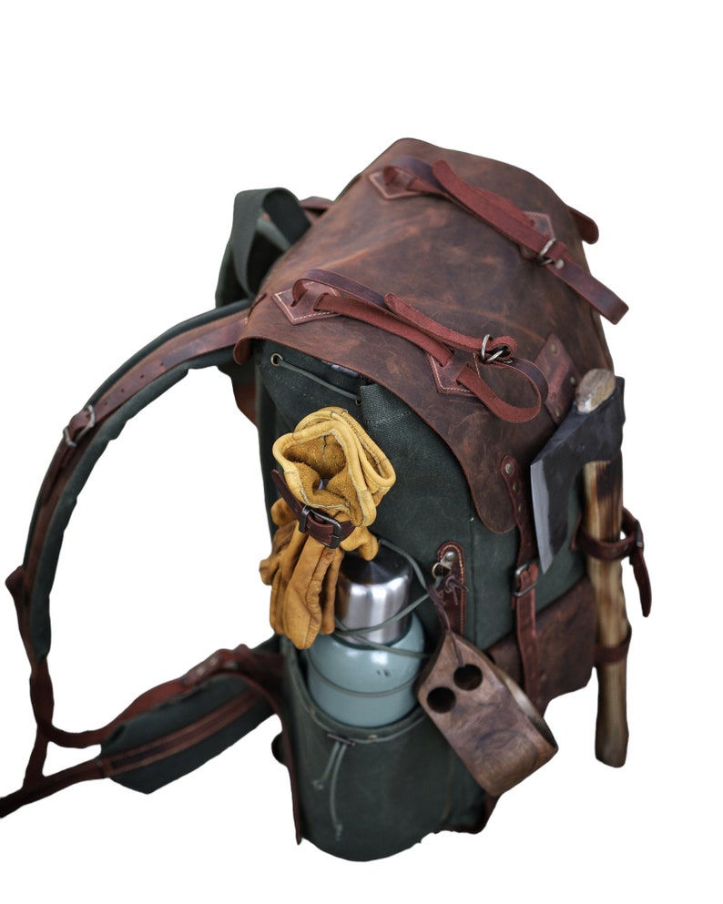 May include: A green canvas and brown leather backpack with a water bottle, gloves, and an axe attached to the outside.