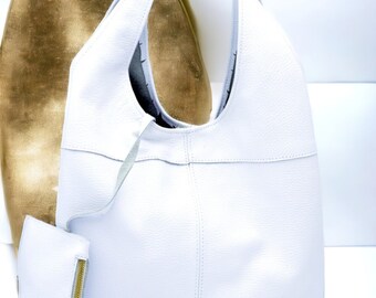May include: A white leather tote bag with a smaller matching zippered pouch. The bag has a slouchy, unstructured design and a single top handle.