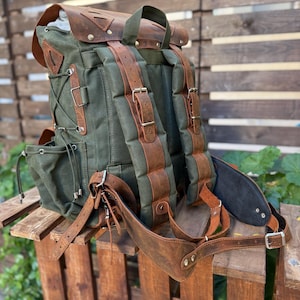 以下が含まれることがあります： 緑色のキャンバスバックパック、茶色の革のアクセント。 調節可能なストラップ、複数のポケット、革製のフラップクロージャーが特徴です。 バックパックは、ハイキングや旅行に最適な、ヴィンテージでアウトドアな美学を持っています。