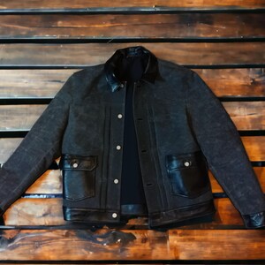 May include: A black denim jacket with a black leather collar and pockets. The jacket has a button closure and a zippered front.