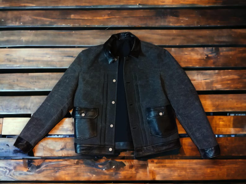 May include: A black denim jacket with a black leather collar and pockets. The jacket has a button closure and a zippered front.