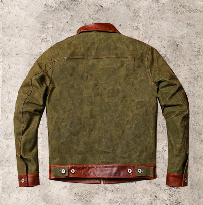 May include: A green canvas jacket with brown leather trim on the collar, cuffs, and bottom hem. The jacket has a button closure and two pockets.