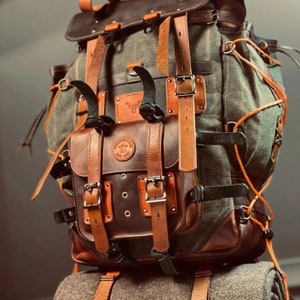 May include: A large, brown leather and canvas backpack with multiple straps and buckles. The backpack has a large front pocket with a flap and buckle closure.